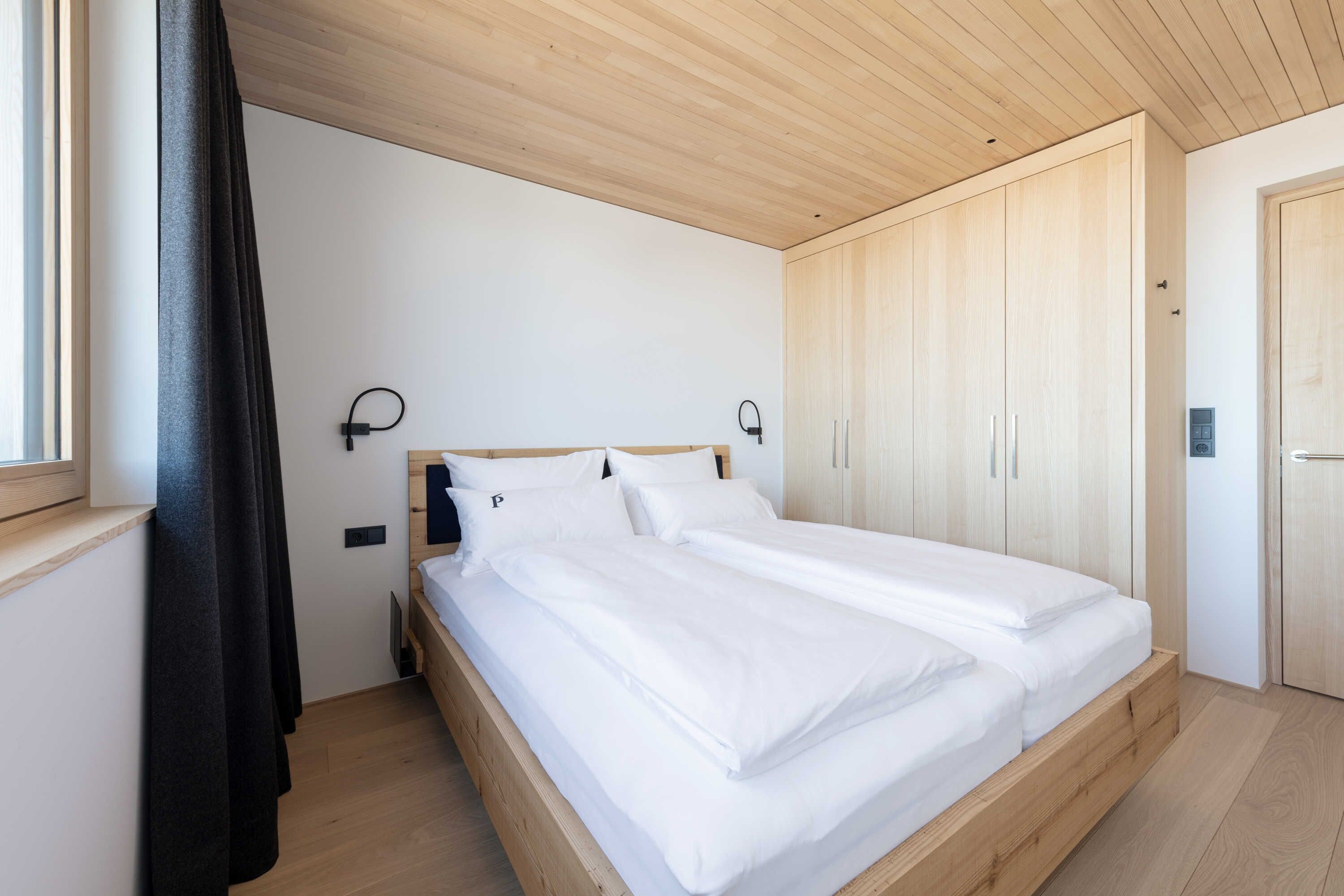 Un dormitorio con cama, armario de madera y ventana con cortinas.