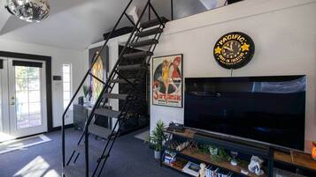 A modern living room with a staircase, a large flat-screen TV, a clock, and a poster.