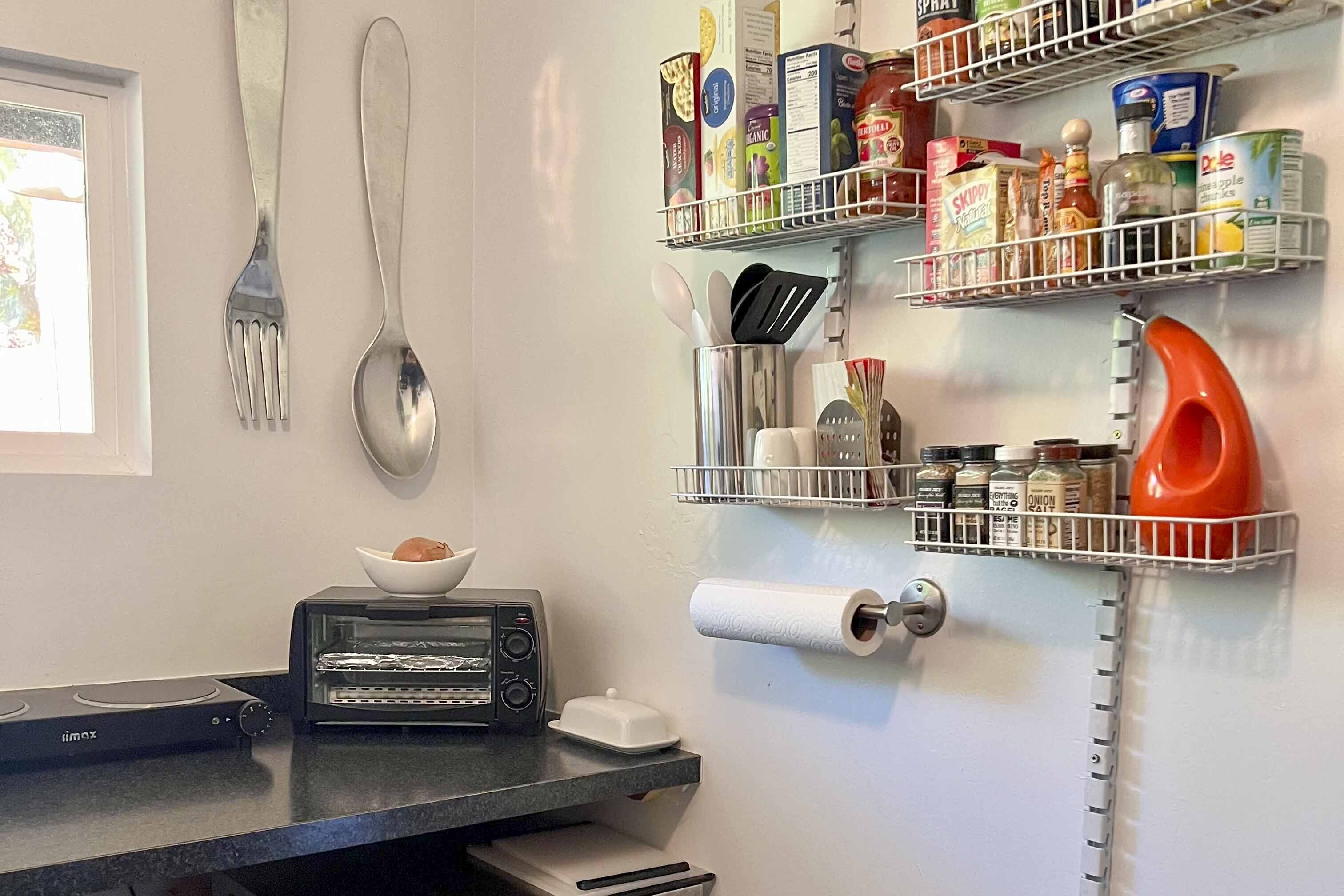 A kitchen with a toaster, a bowl, and a roll of paper towels on the counter. There are shelves above holding various food items and kitchen utensils.