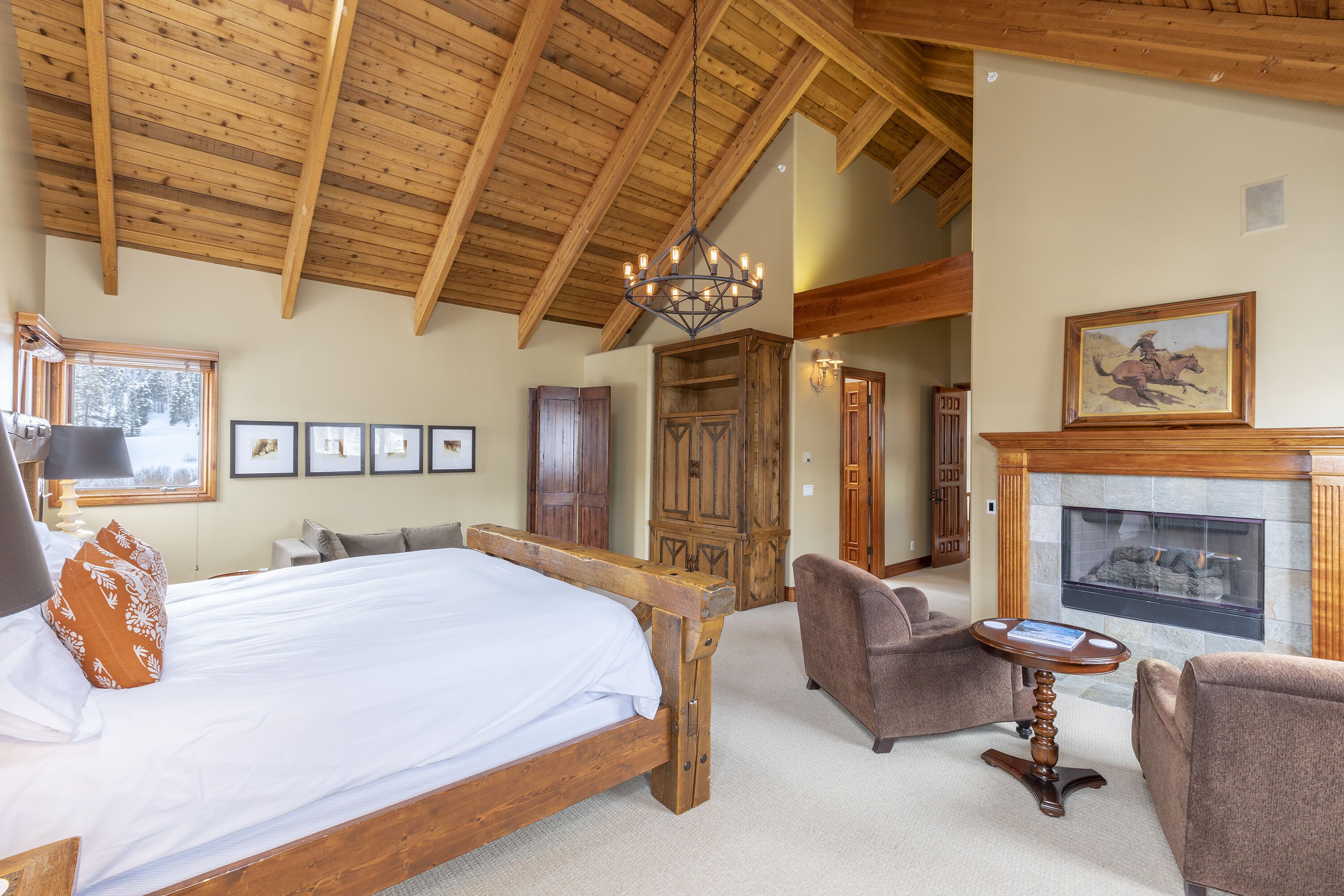 Ruime slaapkamer met een groot bed, houten balken in het plafond, een open haard en een gezellige zithoek met fauteuils.