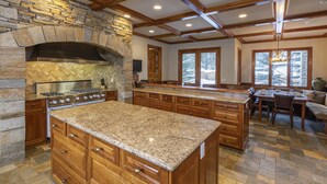 A spacious kitchen with a stone fireplace, wooden cabinets, and a large granite countertop. - GOLD HILL- Spacious, Luxurious Mountain Village Home (Mountain Village)