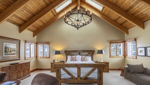 A spacious bedroom with a large bed, wooden ceiling beams, and a chandelier. - GOLD HILL- Spacious, Luxurious Mountain Village Home (Mountain Village)