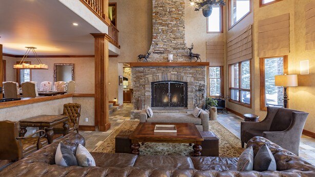 A spacious living room with a stone fireplace, leather furniture, and large windows. - GOLD HILL- Spacious, Luxurious Mountain Village Home (Mountain Village)