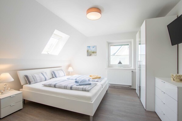 A modern bedroom with a bed, bedside tables, a TV, and a window.