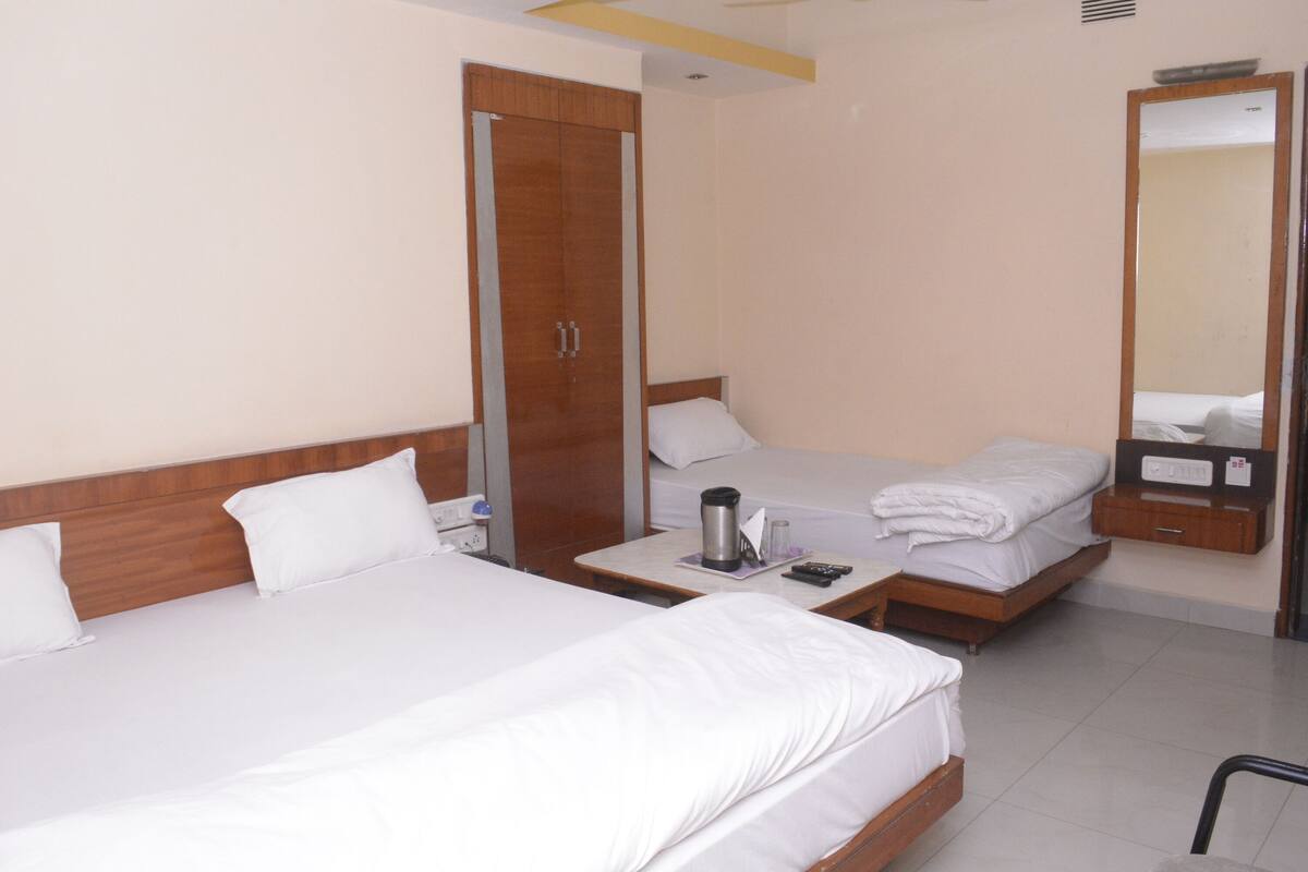 A hotel room with two single beds, a wardrobe, a bedside table with a coffee maker, and a mirror.