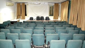 A conference room with rows of chairs, a table, and curtains.