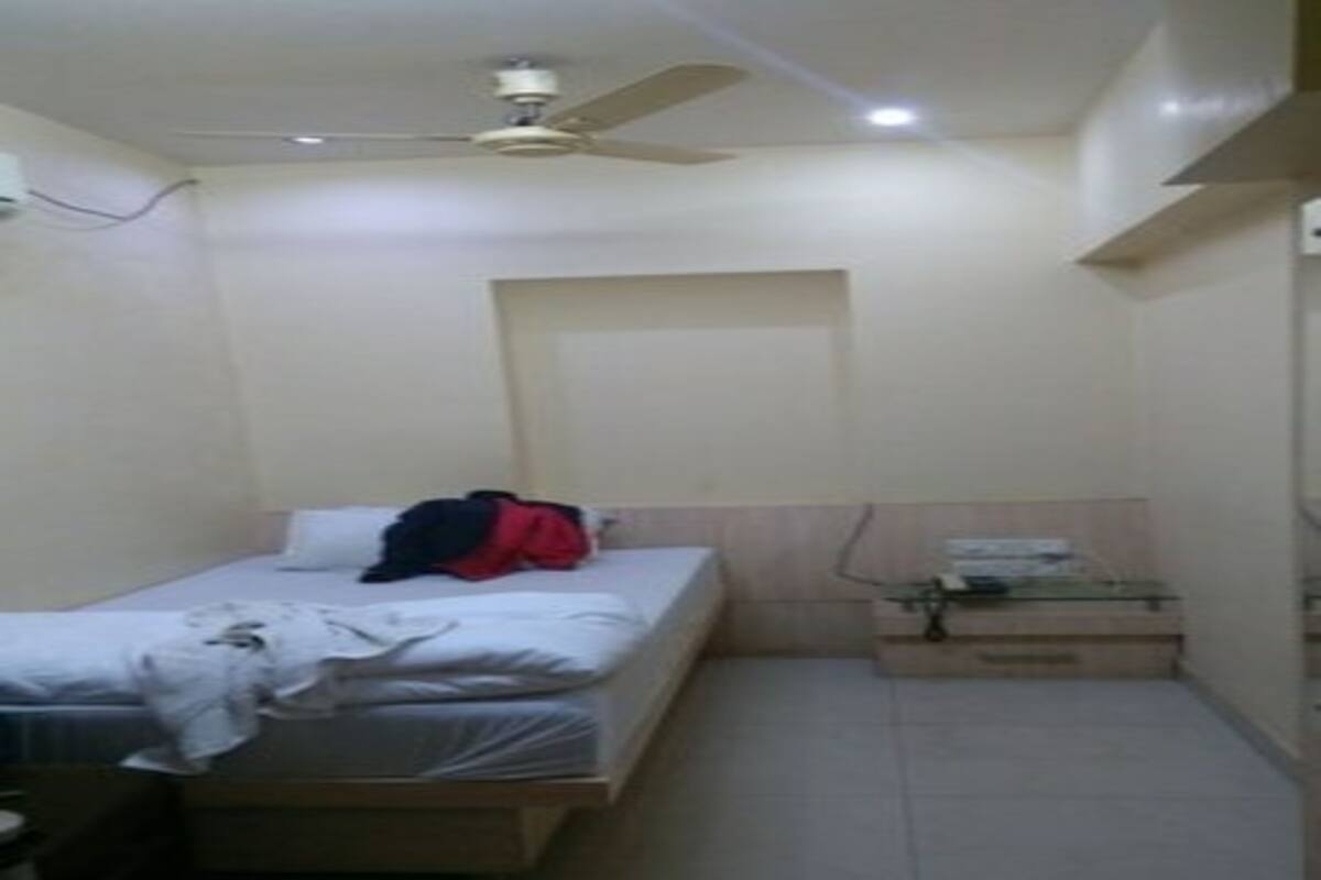 A small, single-bed room with a ceiling fan, a bedside table, and a window with a view of the outside.