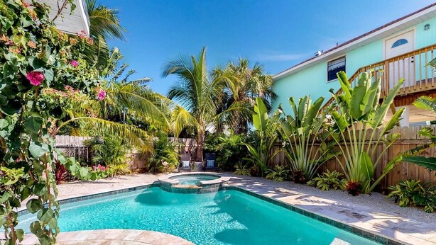 A swimming pool with a curved design, surrounded by tropical plants and a wooden fence. - Over the Moon - By Island Real Estate Vacations (Anna Maria)