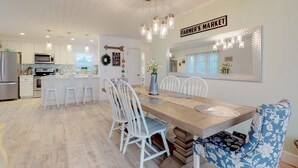 A modern kitchen with white cabinets, a wooden dining table, and a chandelier. - Over the Moon - By Island Real Estate Vacations (Anna Maria)