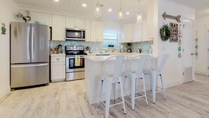 A modern kitchen with white cabinetry, stainless steel appliances, and pendant lighting. - Over the Moon - By Island Real Estate Vacations (Anna Maria)