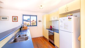 Una cocina compacta con encimera azul, pileta de acero inoxidable, hervidor rojo y refrigerador blanco.
