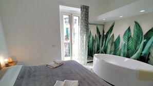 Une chambre à coucher avec un lit, une grande fenêtre, une baignoire et un mur orné d’un motif de feuilles.