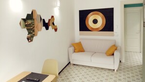 Un salon moderne avec un canapé blanc, une œuvre d’art géométrique accrochée au mur et un sol à motifs.
