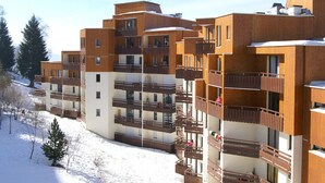 Een meerhoog gebouw met balkons, houten gevel en sneeuw op de grond.