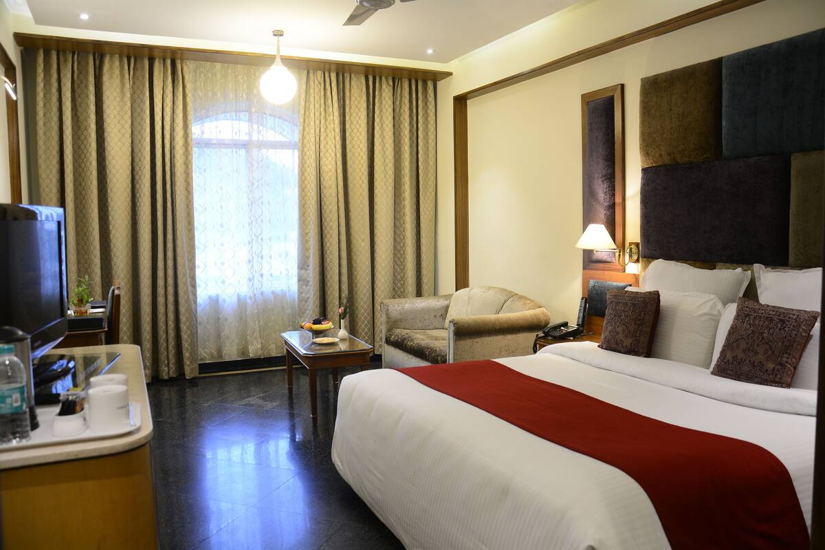 A hotel room with a large bed, a chair, a desk with a lamp, and a TV.
