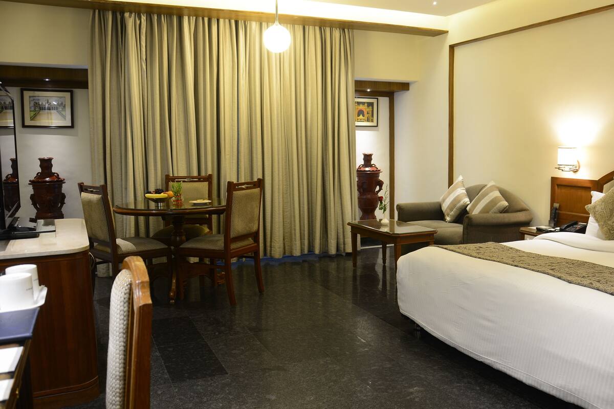 A hotel room with a bed, a desk, a chair, a table, and a large window with curtains.