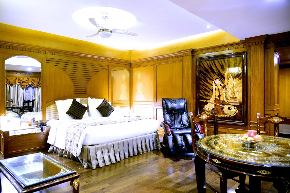A well-appointed hotel room with a large bed, a massage chair, a round table, and a decorative mirror.