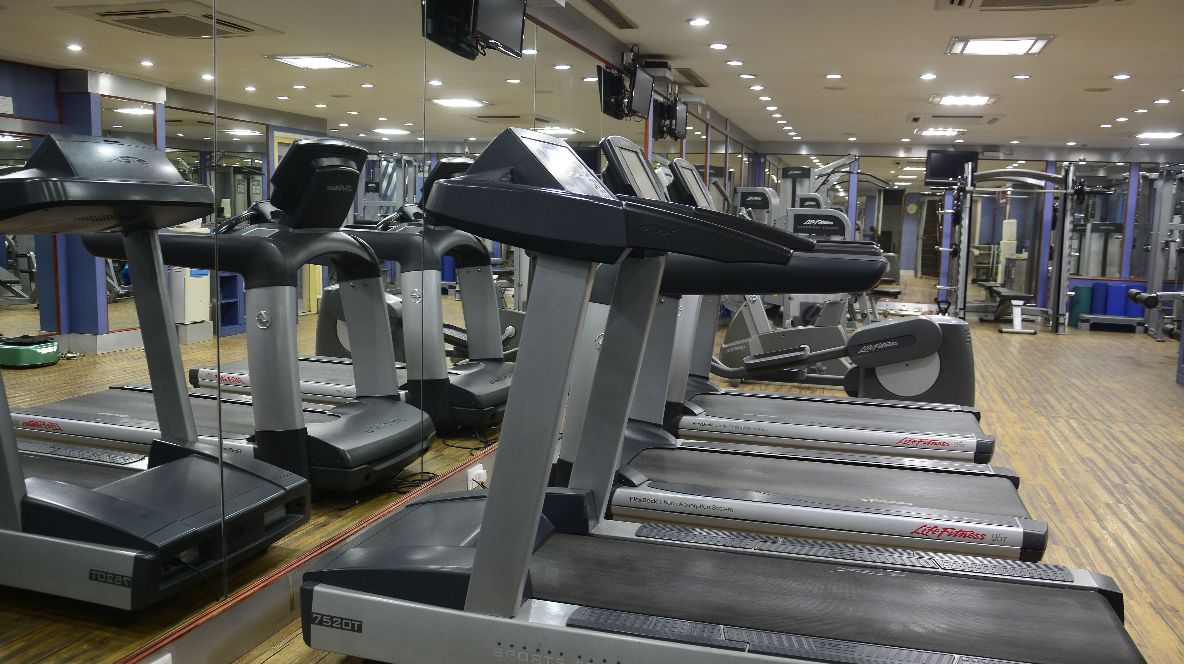 Una hilera de cintas de correr en un gimnasio con paredes de espejo y diversos equipos de ejercicio.