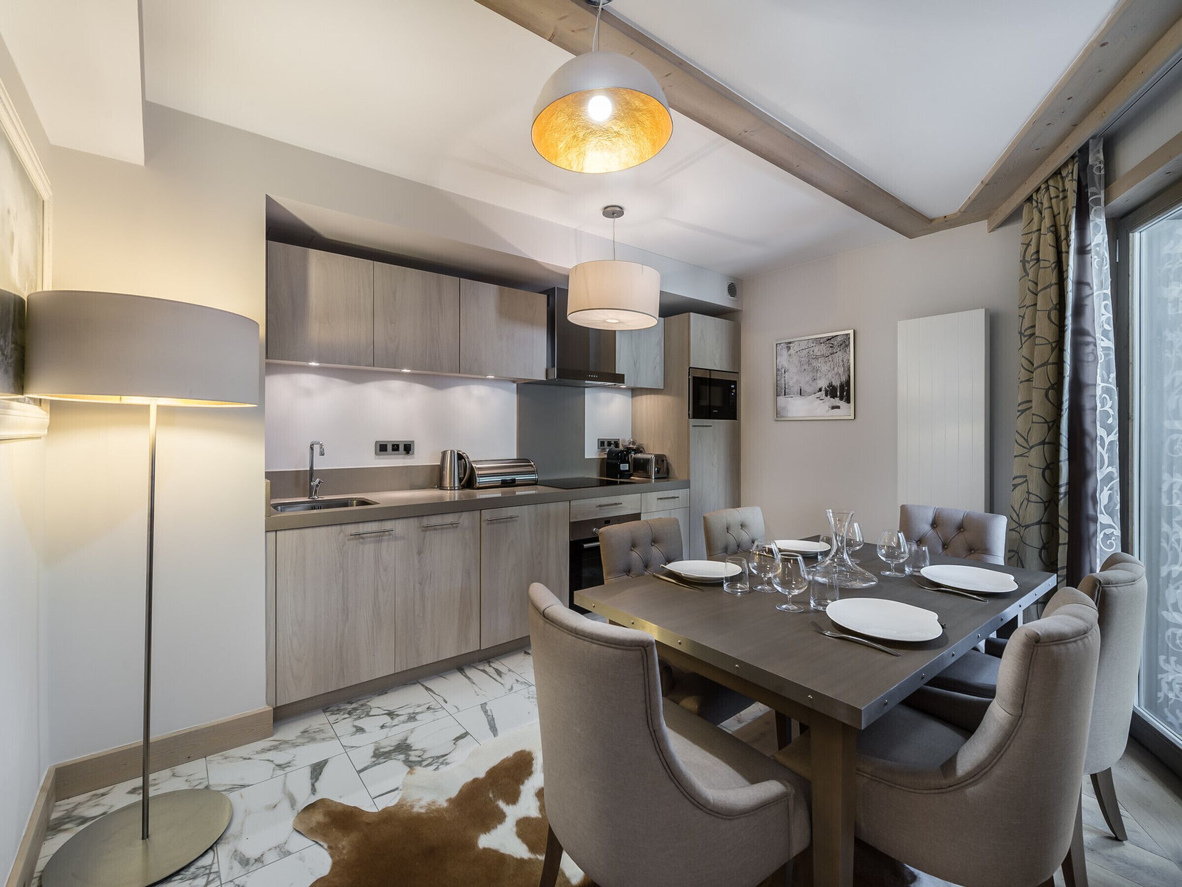 A modern kitchen with built-in appliances, a dining area with a table set for four, and a large window with curtains.