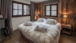 Un dormitorio con una cama grande, paredes de madera y dos ventanas.