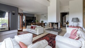 Een ruime woonkamer met een open haard, witte banken en een eethoek.