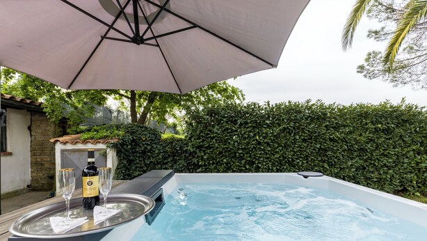 Een jacuzzi met twee champagneglazen en een fles, onder een parasol, omringd door groen.