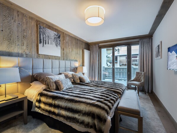 Une chambre d’hôtel moderne, dotée d’un grand lit, d’une banquette, d’un bureau et offrant une vue sur un paysage enneigé par la fenêtre.