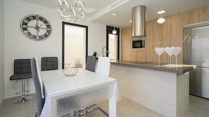 A modern kitchen with a central island, a dining area with a white table and chairs, a wall clock, and pendant lighting. - Villa Barzinu (Isla de Fraile) (Aguilas)
