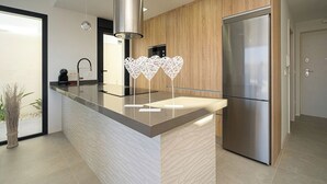 A modern kitchen with a central island, stainless steel appliances, and a wooden accent wall. - Villa Barzinu (Isla de Fraile) (Aguilas)