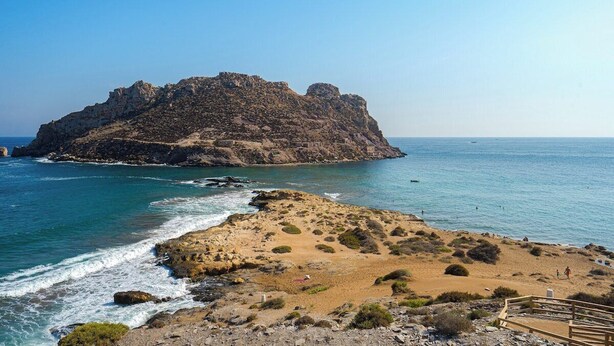 A rocky island with a sandy beach and a wooden walkway leading to it. - Villa Barzinu (Isla de Fraile) (Aguilas)