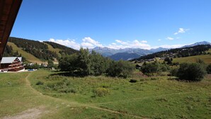 A rural landscape with a clear sky, a path leading to a building with a red roof, and mountains in the background. - Studio cabin 5 pers. with south balcony and GARAGE, Les Saisies (Les Saisies)