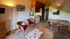 A cozy room with a wooden ceiling, a dining table with chairs, a small kitchen area, and a bed with striped bedding. - Studio cabin 5 pers. with south balcony and GARAGE, Les Saisies (Les Saisies)
