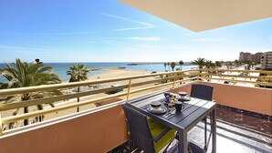 A balcony with a table set for dining, overlooking a beach with palm trees and a clear sky. - Stella Maris - Paseo Maritimo, Fuengirola, Andalucía (Fuengirola)