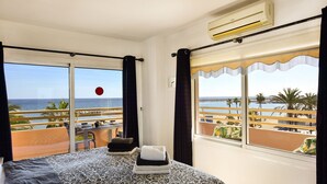 A hotel room with a bed, a table with a chair, and a view of the beach and ocean through large windows. - Stella Maris - Paseo Maritimo, Fuengirola, Andalucía (Fuengirola)