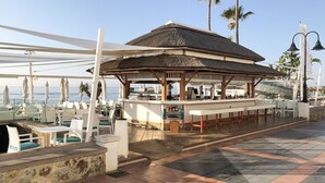 Un bar frente a la playa con terraza y techo de paja.