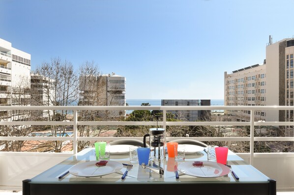 En balkon med et bord dækket til to, med udsigt over bybilleder, bygninger og havet.