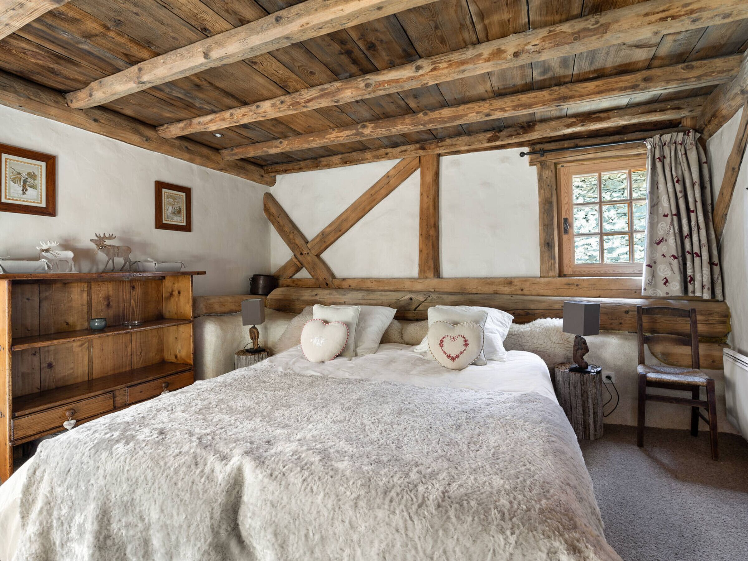 Une chambre à coucher rustique avec des poutres apparentes, une commode en bois, un lit avec une literie blanche et une fenêtre avec des rideaux.