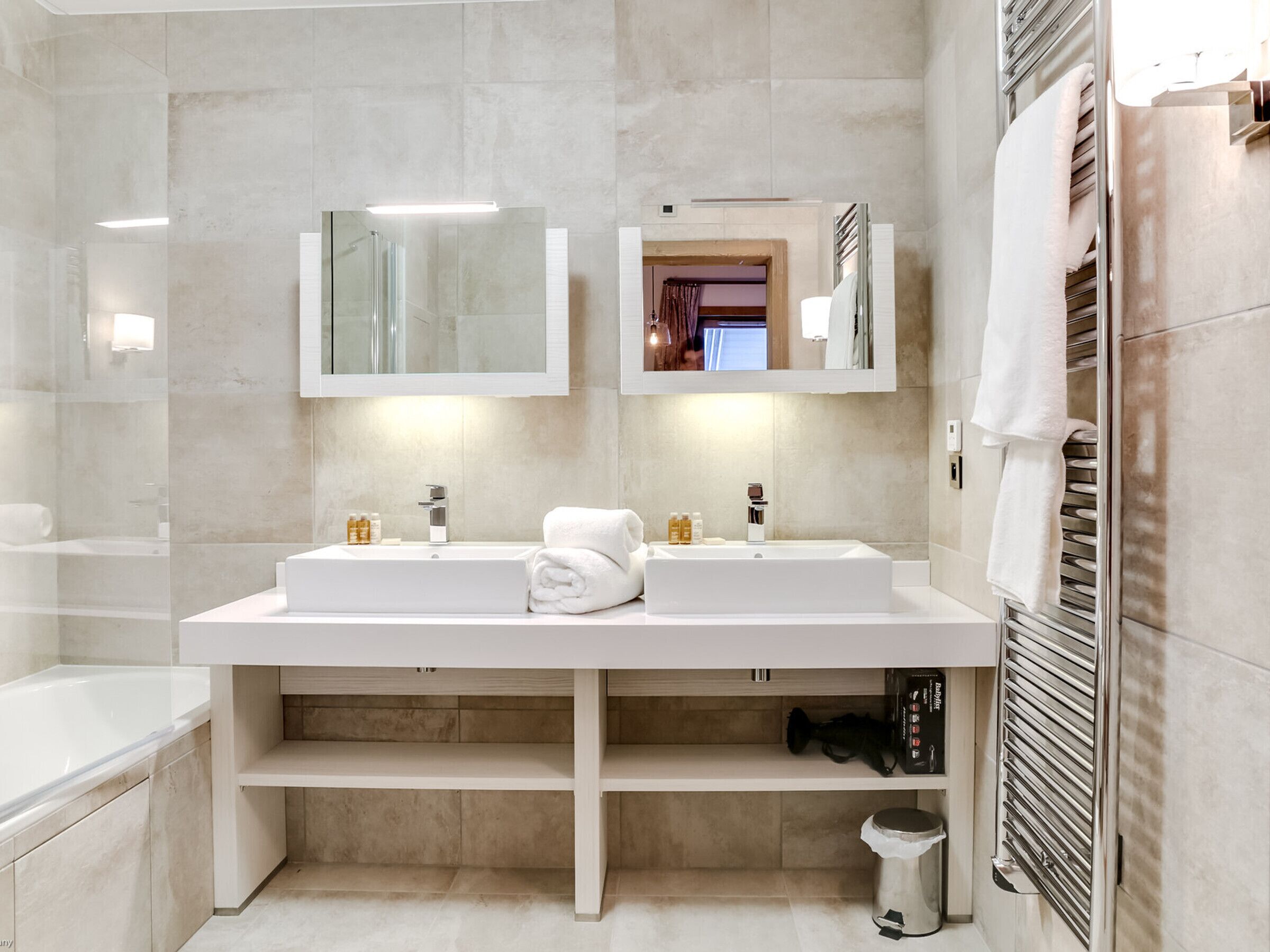 A modern bathroom with two sinks, a mirror, and a towel rack.