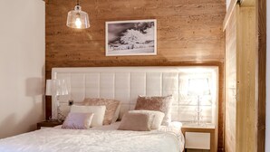 Quarto com teto de madeira, cabeceira branca estofada, espalha roupa de cama branca e fofa e um quadro emoldurado sobre a cama.