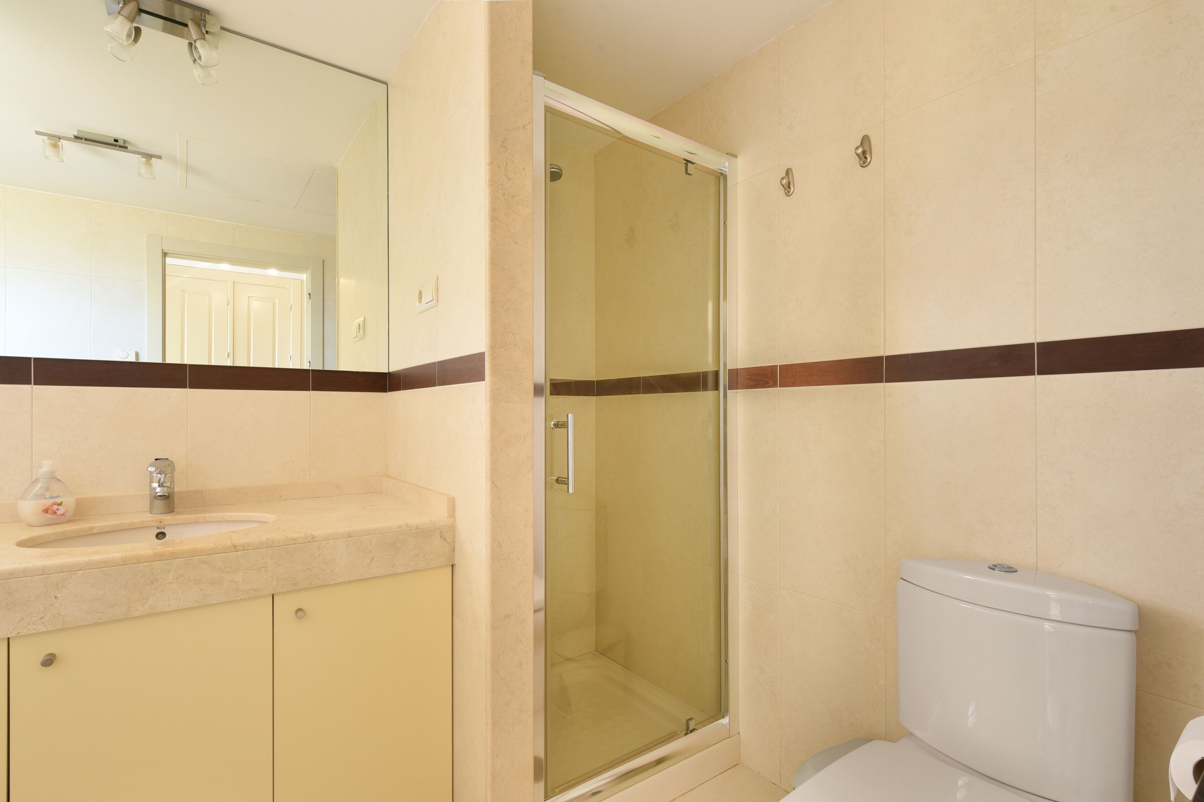 Un baño con ducha de mampara de vidrio, un lavamanos con espejo y un inodoro.