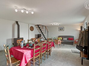 Un coin repas avec une nappe rouge, des chaises en bois, un escalier, un canapé gris et un porte-manteau.