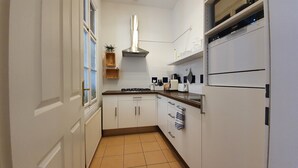 A narrow kitchen with white cabinets, a gas stove, a stainless steel range hood, and a built-in oven. - Gorgeous Viennese Apartment/10 min to City Center (Wien)
