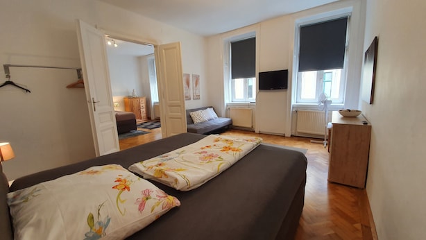 A bedroom with two beds, a sofa, a TV, and a window with blinds. - Gorgeous Viennese Apartment/10 min to City Center (Wien)