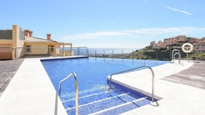 En uendelig pool med krystalklart havudsigt og en bakke med bygninger i baggrunden.