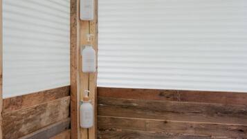Een hoek van een kamer met houten lambrisering en een witte muur. Drie witte flesjes met de aanduiding 'SHAMPOO', 'CONDITIONER' en 'BODY WASH' zijn aan de muur bevestigd.
