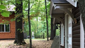 Una cabaña de madera con un porche pequeño, rodeada de árboles y un sendero de tierra.
