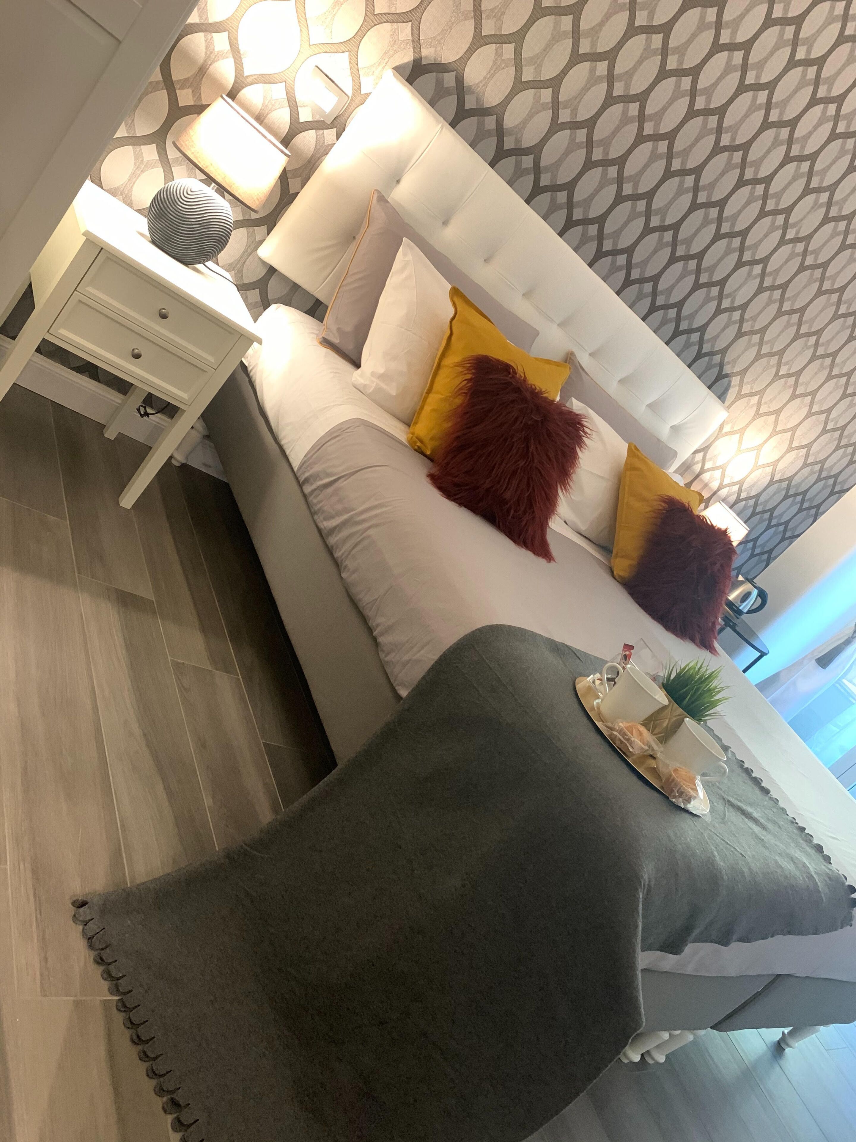 A modern bedroom with a white bed, patterned wallpaper, and a grey throw blanket.