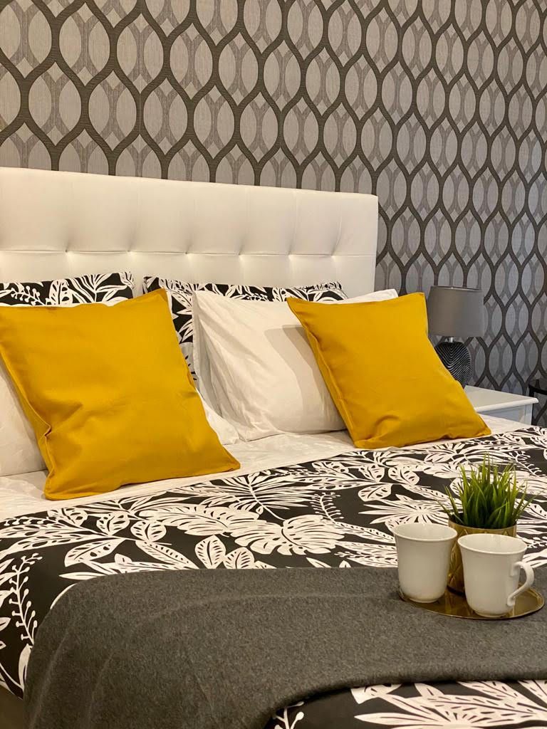 A neatly made bed with a patterned bedspread, two pillows, and a bedside table with a lamp.