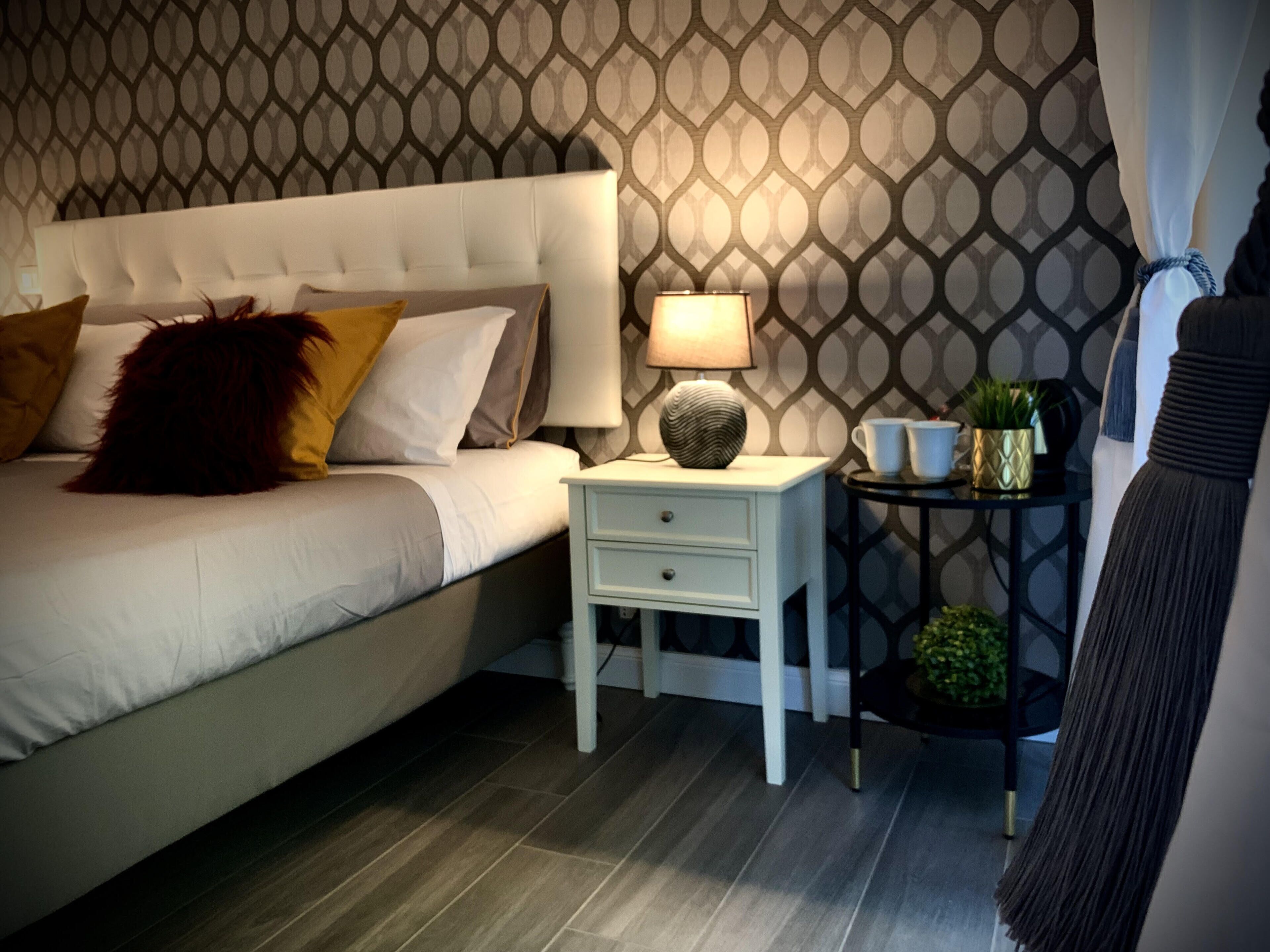 Un dormitorio ordenado con cama, mesita de noche, lámpara y objetos decorativos.