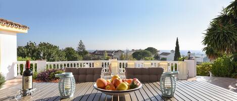 A terrace with a table set for a meal, a bottle of wine, and a bowl of fruit.